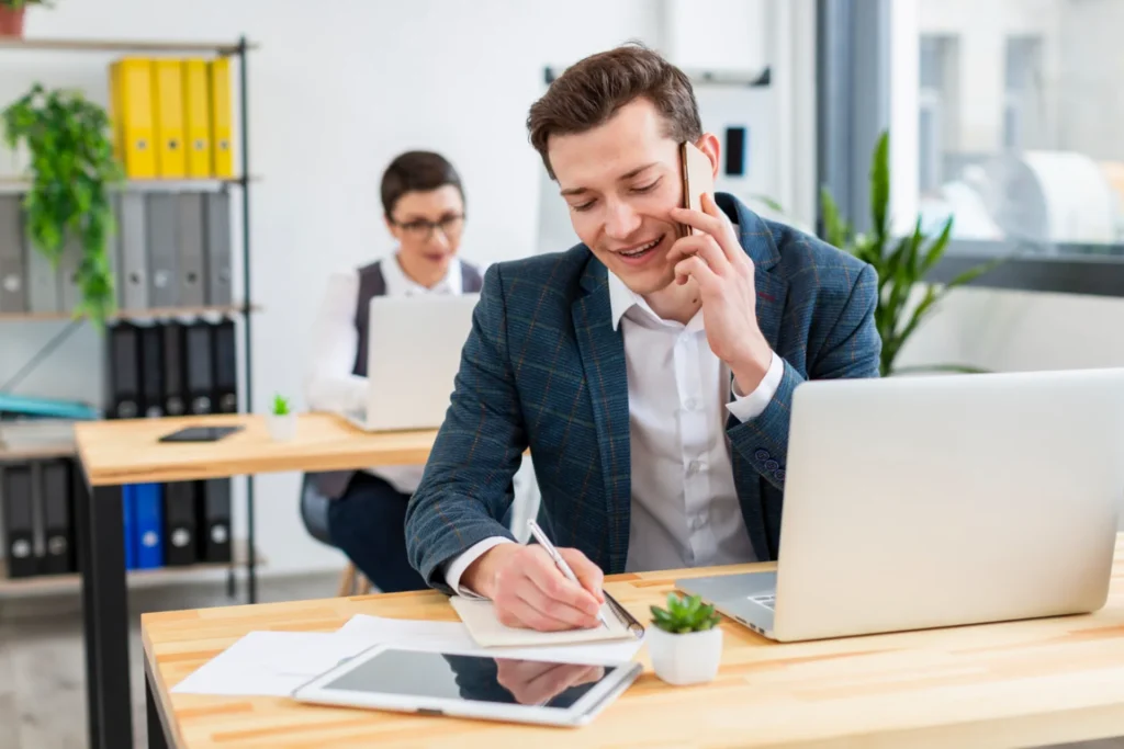 Man talking on phone in office, taking notes.