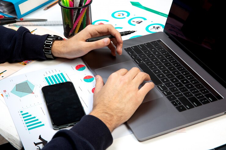 Person analyzing graphs on laptop with smartphone